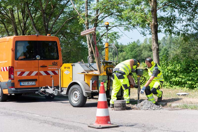 Mitarbeiter von sbt Trier führen Asphaltprüfung mit Bohrgerät am Straßenrand durch